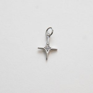 May include: A silver charm in the shape of a four-pointed star with a small clear crystal in the center.