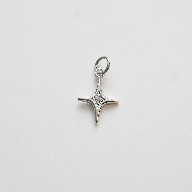 May include: A silver charm in the shape of a four-pointed star with a small clear crystal in the center.