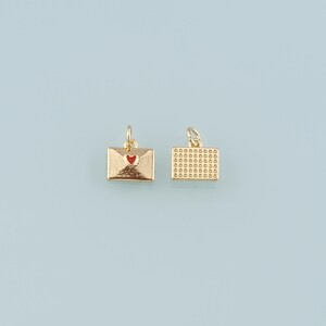 May include: Two gold-colored envelope charms with a textured finish. One charm features a red heart, while the other has a grid pattern. Both charms have a small loop for attaching to jewelry. The background is a light blue.