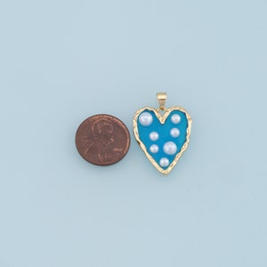 May include: A gold heart-shaped pendant with a blue enamel finish and white pearl accents.