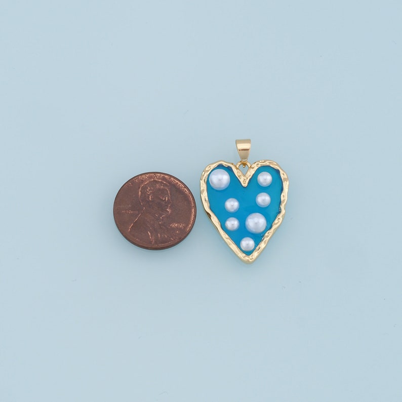 May include: A gold heart-shaped pendant with a blue enamel finish and white pearl accents.