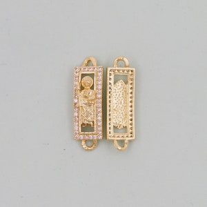 May include: Two gold-toned metal charms in a rectangular shape. One charm features a religious figure in a frame with clear stones. The other charm has a textured design.
