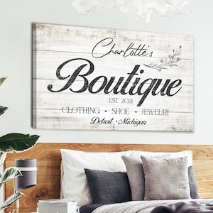 May include: A whitewashed wood sign with black text that reads "Charlotte's Boutique Est. 2021 Clothing Shoe Jewelry Detroit Michigan".