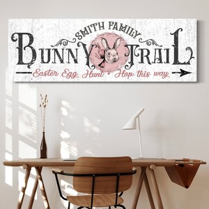 May include: White wooden sign with black text that reads "Smith Family Bunny Trail - Easter Egg Hunt Hop this way" with a pink circle containing a black and white illustration of a bunny rabbit.