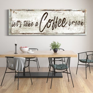 May include: A rustic wooden sign with white paint and black lettering that reads "Let's take a Coffee break". The sign is hanging on a white wall above a dining table with black metal chairs.