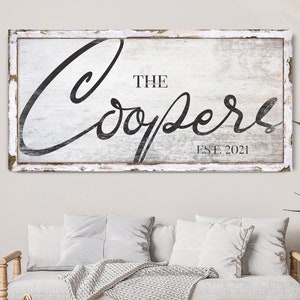 Könnte beinhalten: Ein weißes Holzschild mit schwarzer Schrift, auf dem "The Coopers Est. 2021" steht. Das Schild hat eine weiße, abgenutzte Lackierung und einen weißen Rahmen.