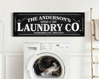 May include: A black and white sign with the text "The Anderson's Wash & Dry Laundry Co. Established 2023 - Open Daily" in a vintage style font. The sign is hanging on a white wall above a white washing machine.