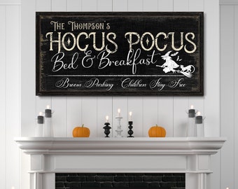 Könnte beinhalten: Ein schwarz-weißes Schild mit dem Text "The Thompson's Hocus Pocus Bed & Breakfast" mit einer Hexe, die auf einem Besen fliegt, und dem Text "Broom Parking Children Stay Free". Das Schild hängt über einem weißen Kamin mit einem schwarzen Ziegelinneren. Auf dem Kaminsims stehen orangefarbene Kürbisse und Kerzen.