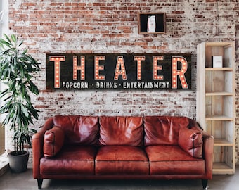 May include: A black and red sign with white lettering that reads "THEATER POPCORN - DRINKS - ENTERTAINMENT". The sign has light bulbs around the letters and is hanging on a brick wall.