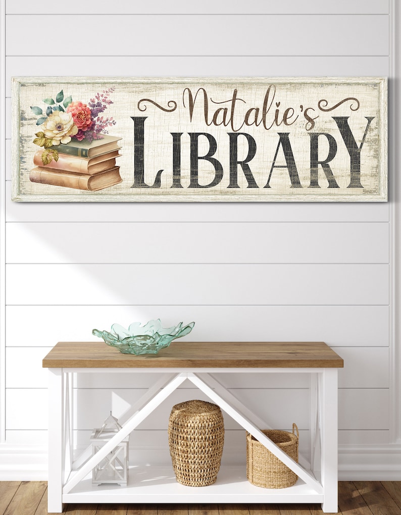Pu&ograve; includere: Un cartello in legno bianco con una finitura usurata, decorato con un motivo floreale e il testo "Natalie's LIBRARY".