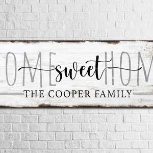 May include: White wooden sign with the text "Home sweet Home" in black cursive lettering and "The Cooper Family" in gray lettering below.
