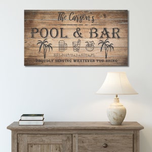 May include: A wooden sign with the text "The Carson's Pool & Bar Est. 2017/Sarasota, FL Proudly Serving Whatever You Bring". The sign features palm trees, a beer mug, a glass of iced tea, and a coconut with a straw.