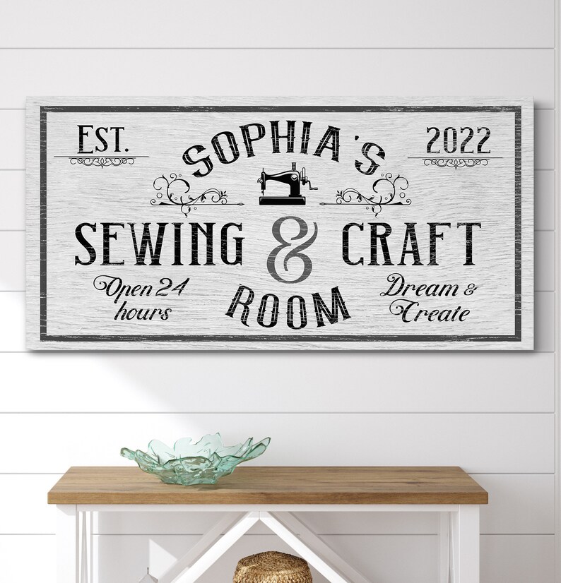 Puede incluir: Un letrero de madera blanco con texto negro que dice "EST. 2022 SOPHIA'S SEWING & CRAFT ROOM Open 24 hours Dream & Create". Una ilustraci&oacute;n en blanco y negro de una m&aacute;quina de coser est&aacute; sobre el texto.