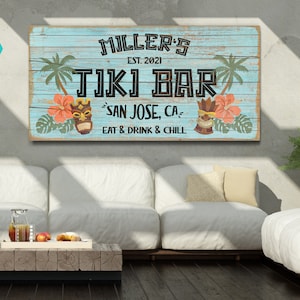 K&ouml;nnte beinhalten: Ein blaues und wei&szlig;es Holzschild mit dem Text "MILLER'S EST. 2021 TIKI BAR SAN JOSE, CA EAT & DRINK & CHILL". Das Schild hat ein tropisches Thema mit Palmen, Blumen und Tiki-Masken.