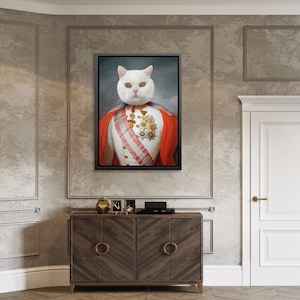 May include: A white cat dressed in a red and white military uniform with gold accents. The cat is wearing a crown and has a serious expression on its face. The image is framed and hanging on a wall.