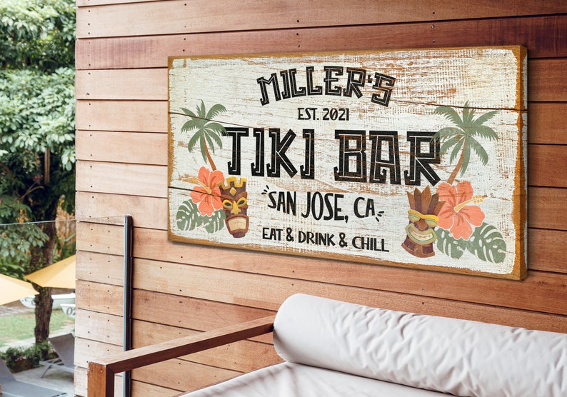 K&ouml;nnte beinhalten: Ein wei&szlig;es Holzschild mit dem Text "MILLER'S EST. 2021 TIKI BAR SAN JOSE, CA EAT & DRINK & CHILL" in schwarzer Schrift. Das Schild ist mit Palmen, Hibiskusbl&uuml;ten und Tiki-Masken verziert.