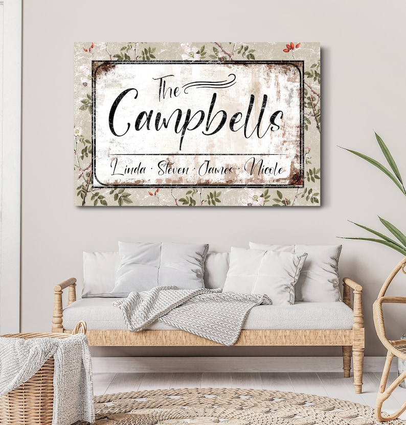 Op de afbeelding: Een rechthoekig familienaambord met de naam "The Campbells" in sierlijk schrift. Daaronder staan de namen "Linda, Steven, James, Nicole" vermeld. De achtergrond heeft een verweerde, vintage uitstraling met bloemaccenten.