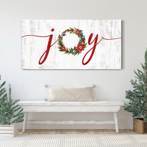 May include: White wooden sign with the word "joy" written in red cursive lettering. A red and green Christmas wreath with red berries and white flowers is incorporated into the letter "o".