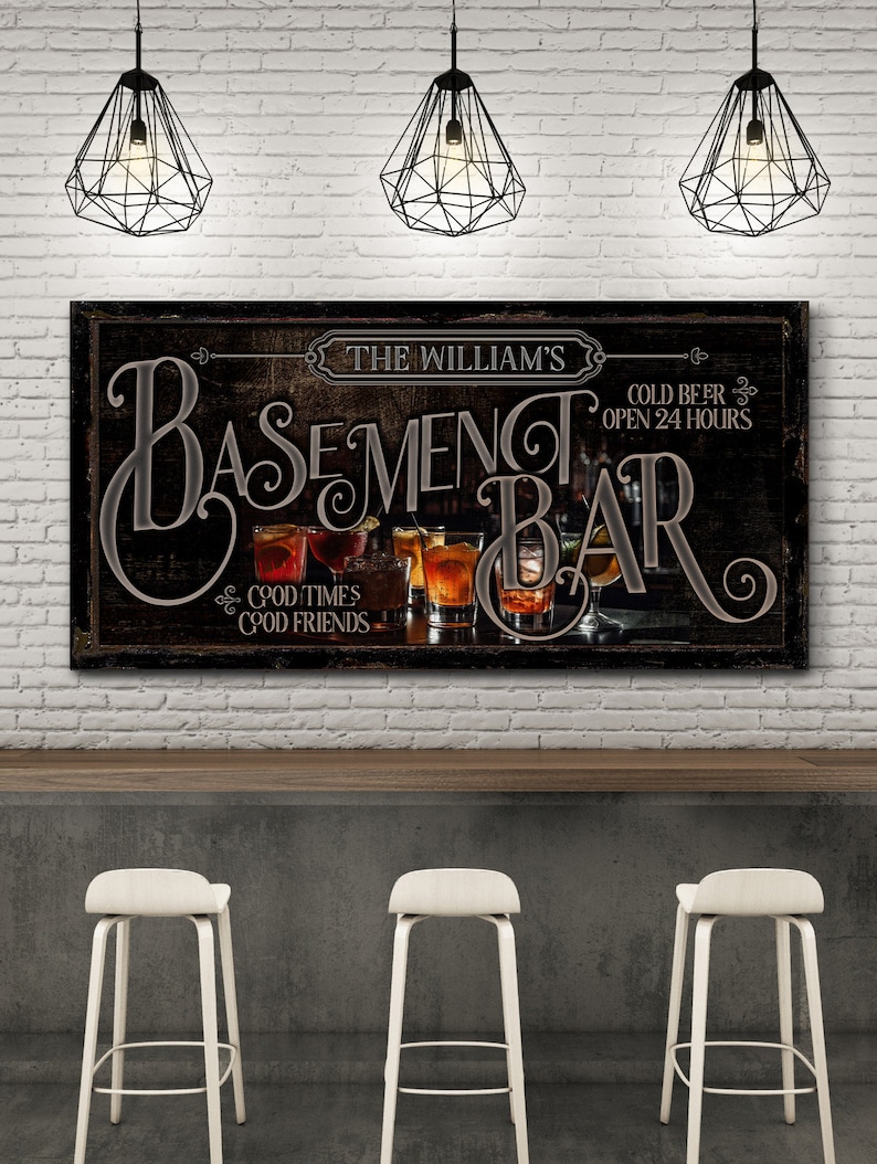 May include: A black and brown sign with the text "The William's Basement Bar" and "Cold Beer Open 24 Hours". The sign also has the text "Good Times Good Friends" and features a variety of drinks in glasses.
