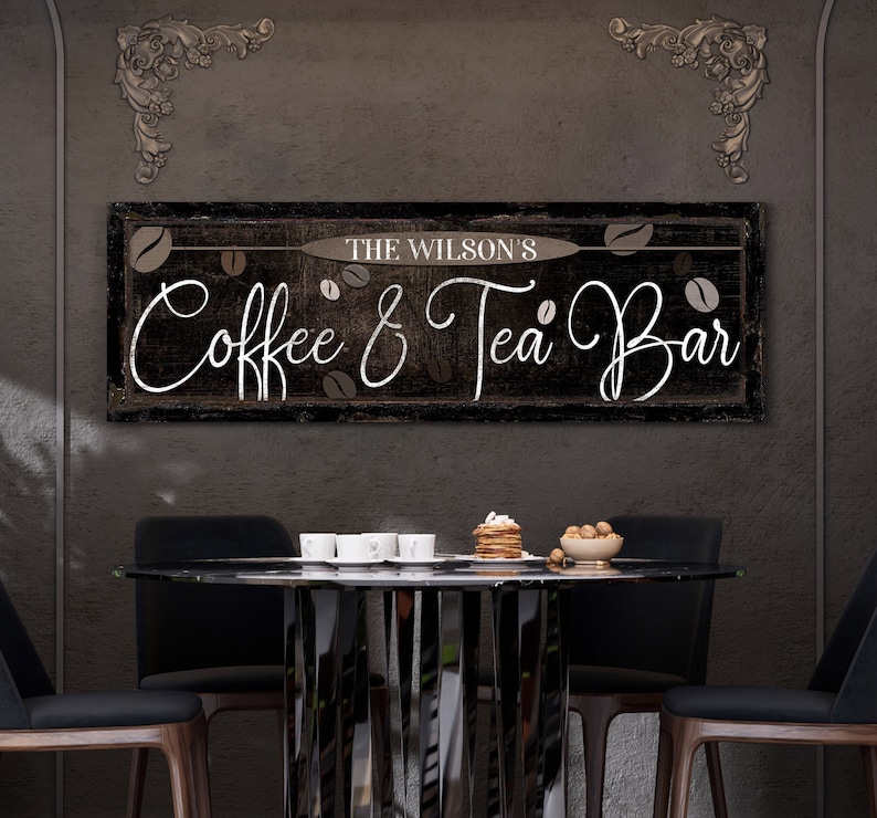 May include: A black and white sign with the text "The Wilson's Coffee & Tea Bar" in a cursive font. The sign is hanging on a dark gray wall above a black table with four chairs.