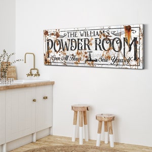 May include: Rustic white sign with black text that reads "The William's Powder Room Open All Hours Seat Yourself". The sign has a distressed look with rust accents.