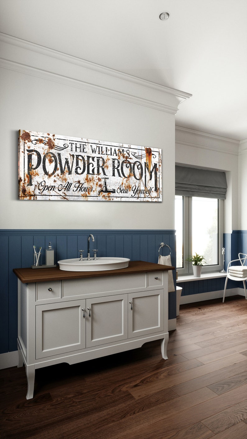 May include: A white bathroom vanity with a brown countertop and three drawers. A white porcelain sink with a chrome faucet is on the countertop. A rusty metal sign above the vanity reads "The Williams' Powder Room Open All Hours Seat Yourself".