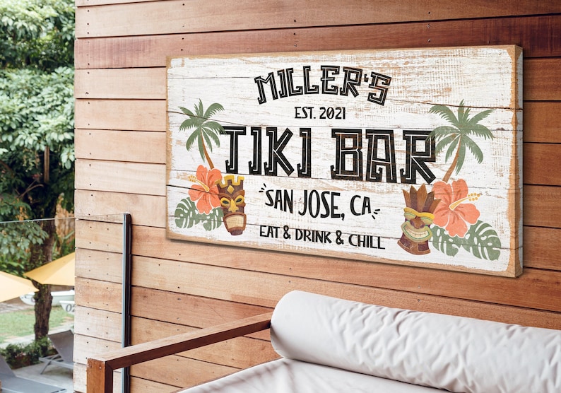 K&ouml;nnte beinhalten: Ein wei&szlig;es Holzschild mit schwarzem Text, der "MILLER'S EST. 2021 TIKI BAR SAN JOSE, CA EAT & DRINK & CHILL" lautet. Das Schild ist mit tropischen Pflanzen, Blumen und Tiki-Masken verziert.