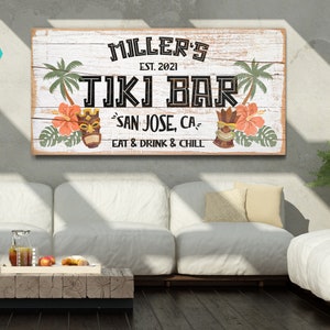 K&ouml;nnte beinhalten: Ein wei&szlig;es Holzschild mit dem Text "MILLER'S EST. 2021 TIKI BAR SAN JOSE, CA EAT & DRINK & CHILL". Das Schild hat ein tropisches Thema mit Palmen, Blumen und Tiki-Masken.