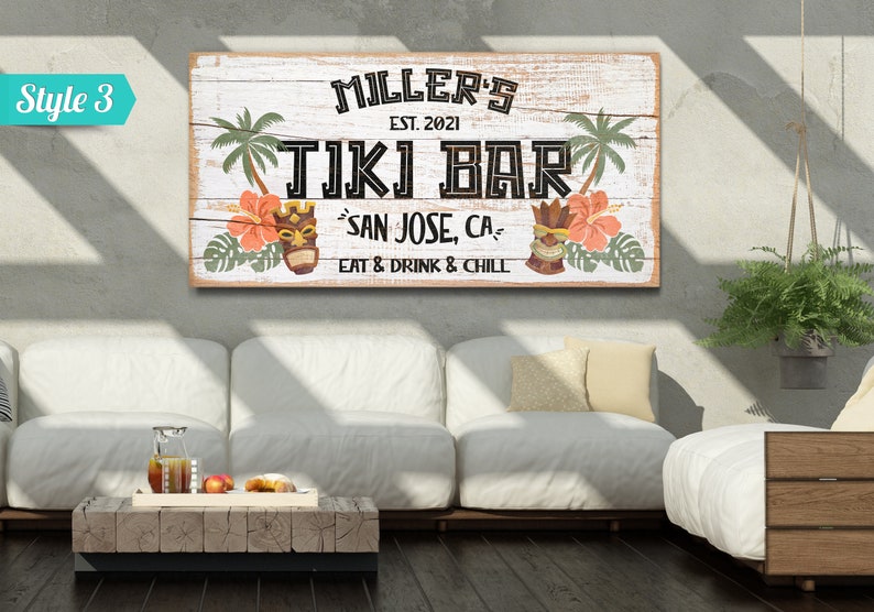 K&ouml;nnte beinhalten: Ein wei&szlig;es Holzschild mit dem Text "MILLER'S EST. 2021 TIKI BAR SAN JOSE, CA EAT & DRINK & CHILL". Das Schild hat ein tropisches Thema mit Palmen, Blumen und Tiki-Masken.