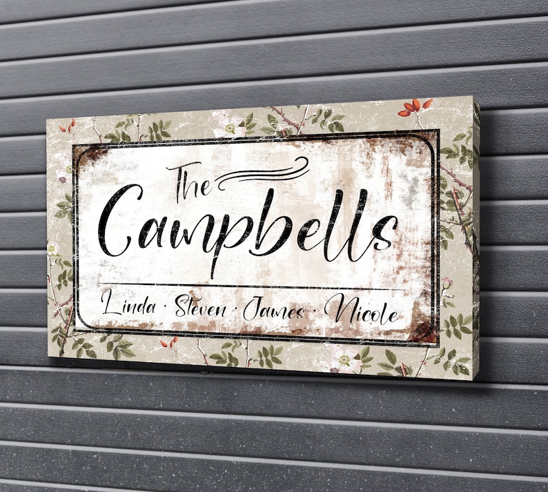 Op de afbeelding: Een rechthoekig familienaambord met de tekst "The Campbells" in sierlijk schrift. Daaronder staan de namen Linda, Steven, James en Nicole. Het bord heeft een verweerde, vintage uitstraling met bloemmotieven.