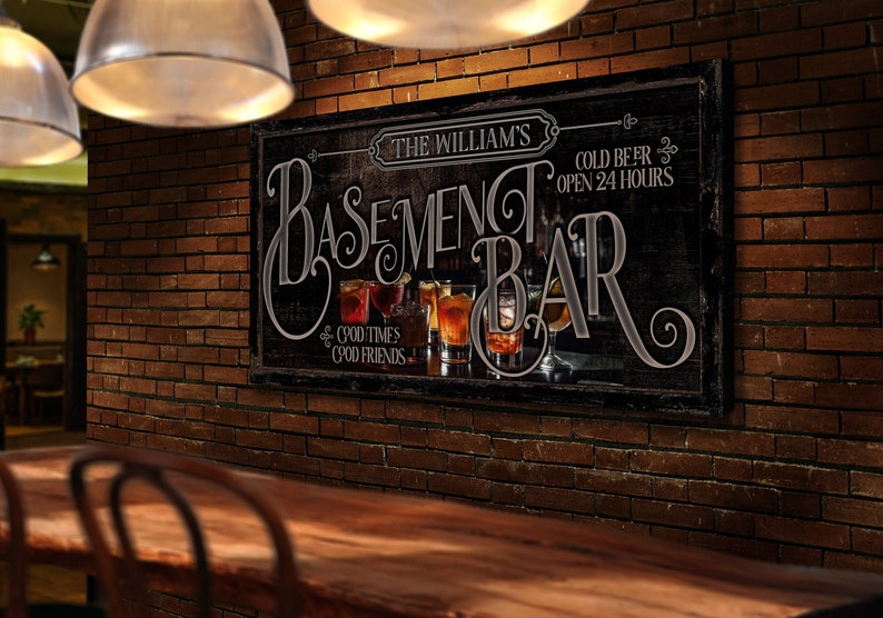 May include: A black and white sign with the text "The William's Basement Bar" and "Cold Beer Open 24 Hours". The sign has a vintage look and features a row of glasses with drinks.