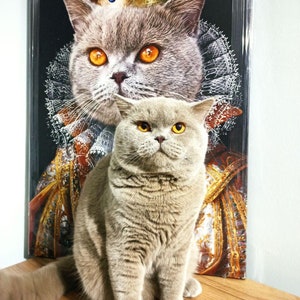 May include: A gray cat wearing a gold crown sits in front of a painting of a gray cat wearing a gold crown. The cat in the painting is wearing a red and gold robe.