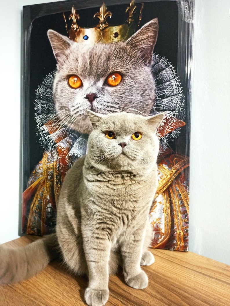 May include: A gray cat wearing a gold crown sits in front of a painting of a gray cat wearing a gold crown. The cat in the painting is wearing a red and gold robe.