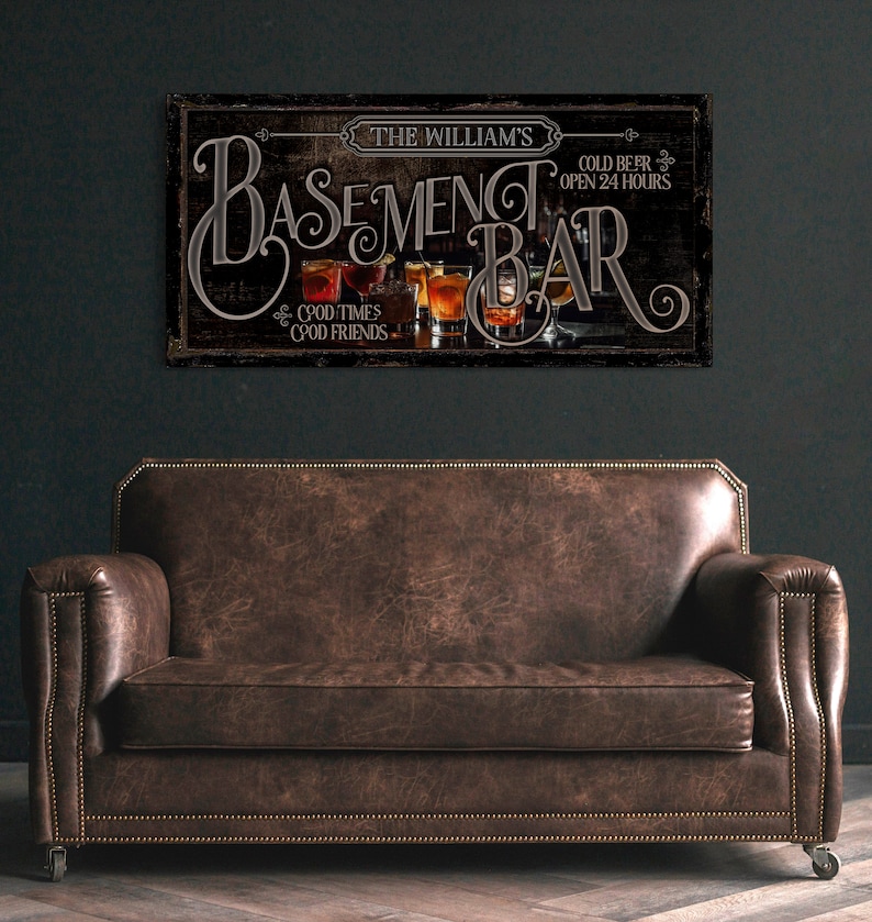 May include: A rustic wooden sign with the text "The William's Basement Bar" in a stylized font. The sign features a depiction of glasses of beer and the text "Cold Beer Open 24 Hours" and "Good Times Good Friends".