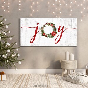 May include: White wooden sign with the word "joy" written in red cursive script. A red and green Christmas wreath with red berries is incorporated into the word "joy".