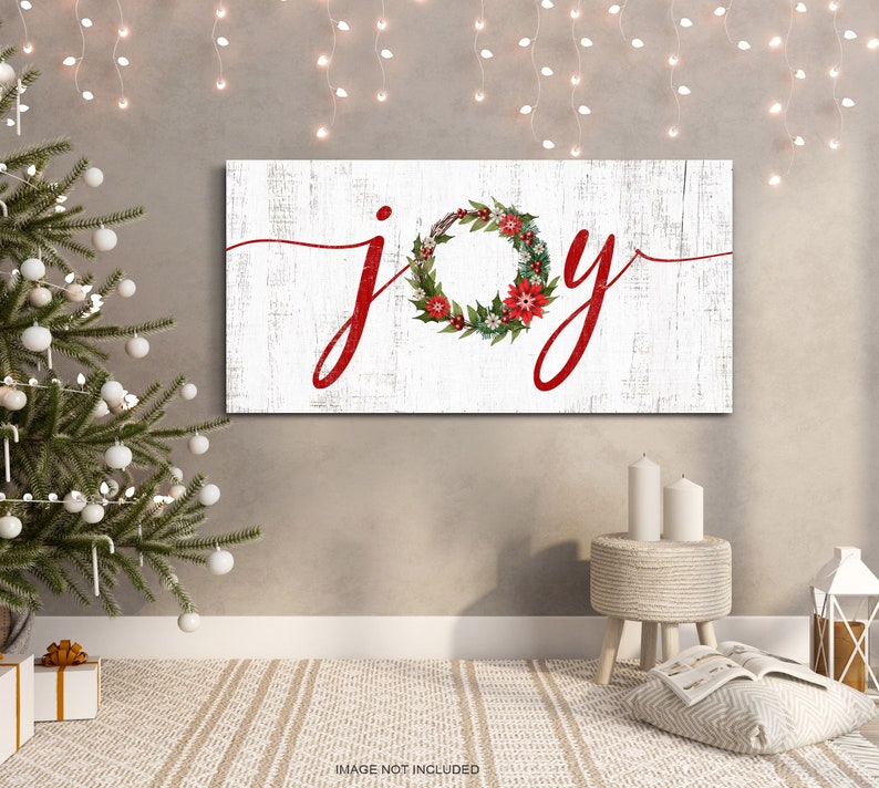 May include: White wooden sign with the word "joy" written in red cursive script. A red and green Christmas wreath with red berries is incorporated into the word "joy".