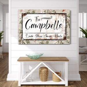 Op de afbeelding: Een rechthoekig familienaambord met de tekst "The Campbells" in elegant schrift. Het bord bevat de namen Linda, Steven, James en Nicole. De achtergrond heeft een bloemenpatroon met een verweerde, vintage uitstraling.