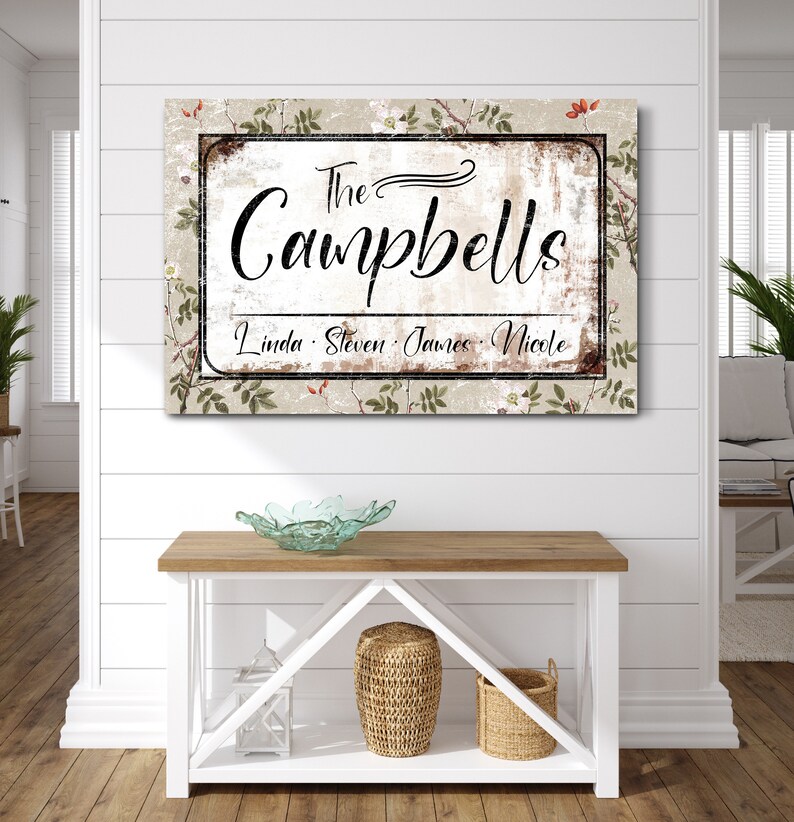 Op de afbeelding: Een rechthoekig familienaambord met de tekst "The Campbells" in elegant schrift. Het bord bevat de namen Linda, Steven, James en Nicole. De achtergrond heeft een bloemenpatroon met een verweerde, vintage uitstraling.