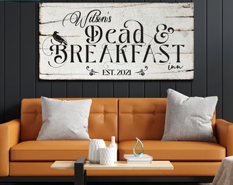 May include: A white wooden sign with black text that reads "Wilson's Dead & Breakfast Inn Est. 2021". A black crow silhouette is to the left of the text.