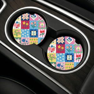 May include: Two circular car cup holder coasters featuring a colorful patchwork quilt design. Each coaster displays a grid of squares with various floral patterns, gingham checks, and geometric shapes in shades of pink, blue, yellow, and red.