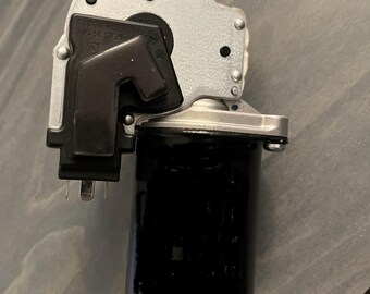 Può includere: Un componente automobilistico argentato e nero. Il componente presenta un elemento cilindrico nero collegato a un telaio metallico argentato. Il telaio ha diversi fori e un pezzo di plastica nera. Il testo "CZECH REPUBLIC" è visibile sul componente.