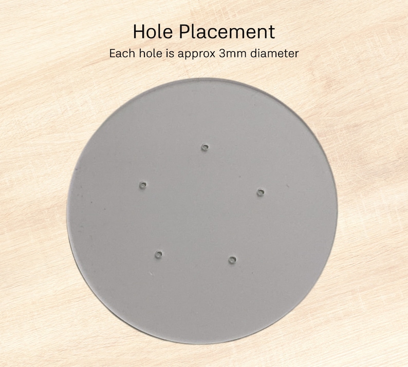Puede incluir: Un objeto circular gris con cinco peque&ntilde;os agujeros espaciados uniformemente. El texto "Hole Placement" y "Each hole is approx 3mm diameter" son visibles. El objeto est&aacute; sobre una superficie de madera clara.