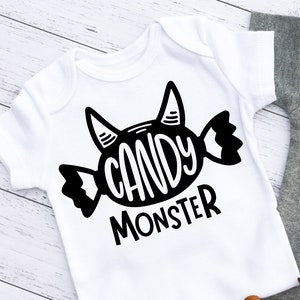 Puede incluir: Dos bodies de bebé blancos y grises con texto negro que dice "Candy Monster" y un gráfico de caramelo negro con cuernos de diablo.