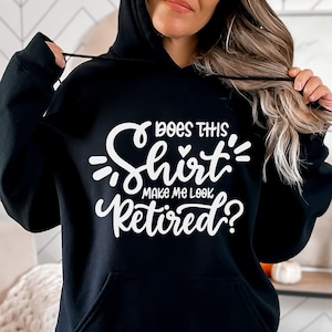 Op de afbeelding: Zwart hoodie met witte tekst die "Does this shirt make me look retired?" zegt.