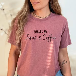 May include: A mauve t-shirt with the text "Fueled by: Jesus & Coffee" printed in black.