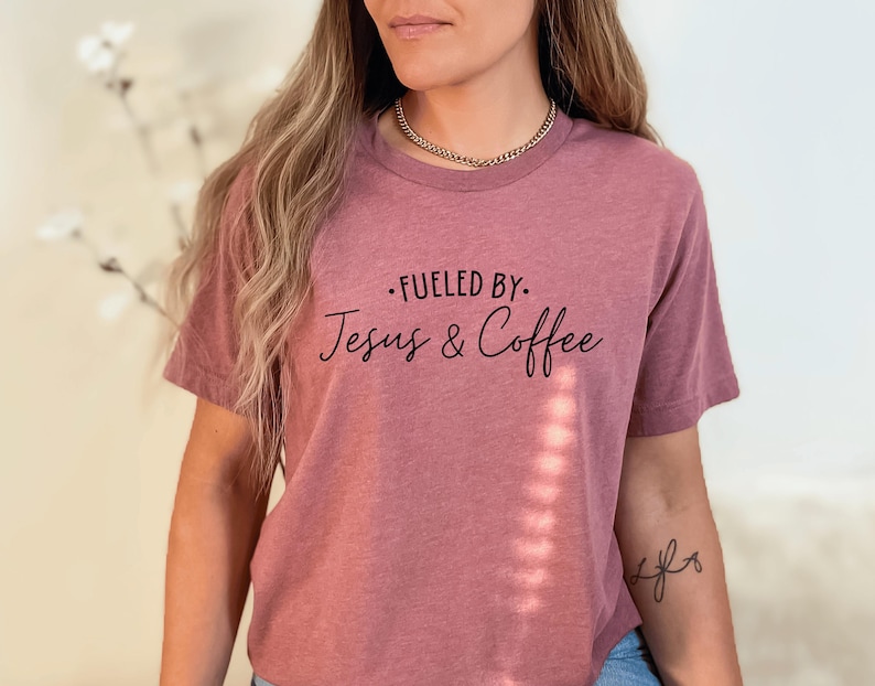 May include: A mauve t-shirt with the text "Fueled by: Jesus & Coffee" printed in black.
