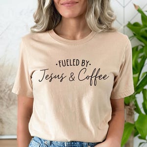 May include: A beige t-shirt with the text "Fueled by: Jesus & Coffee" printed in black.