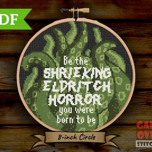 Op de afbeelding: Groene en zwarte kruissteek borduurring met de tekst "Be the Shrieking Eldritch Horror you were born to be" en "8-inch Circle".
