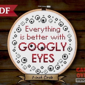 以下が含まれることがあります： 黒と白のググリーアイで囲まれた赤いテキスト「Everything is better with GOOGLY EYES」が特徴のクロスステッチパターン。このパターンは、18cmの刺繍枠用に設計されています。