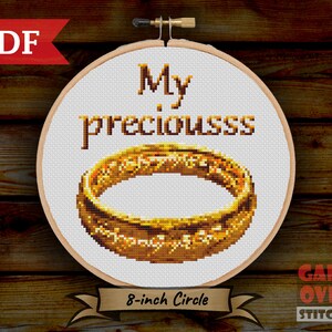 May include: An 8-inch round embroidery hoop with white fabric stretched across it. The fabric has a gold embroidered image of the One Ring from The Lord of the Rings and the text "My preciousss".